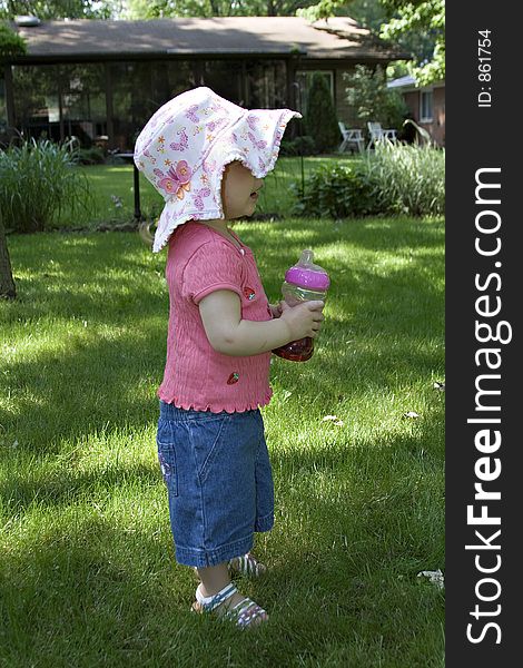 Small baby, toddler girl playing in yard wearing sun hat and sandles with cup of juice in hand. Small baby, toddler girl playing in yard wearing sun hat and sandles with cup of juice in hand.