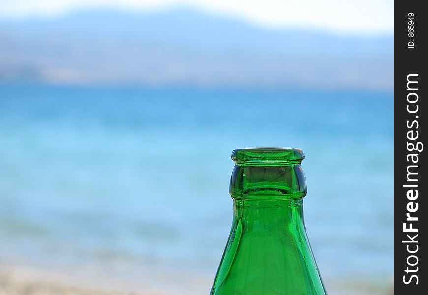 The top of a green beer bottle, against a blue sea background. The top of a green beer bottle, against a blue sea background