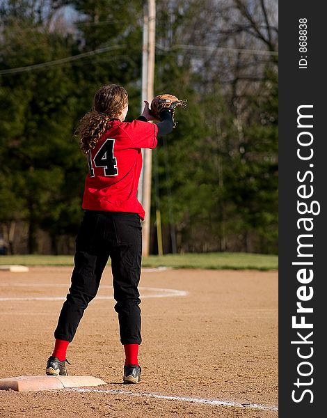 Female softball player. First baseman wearing black pants and a red shirt.