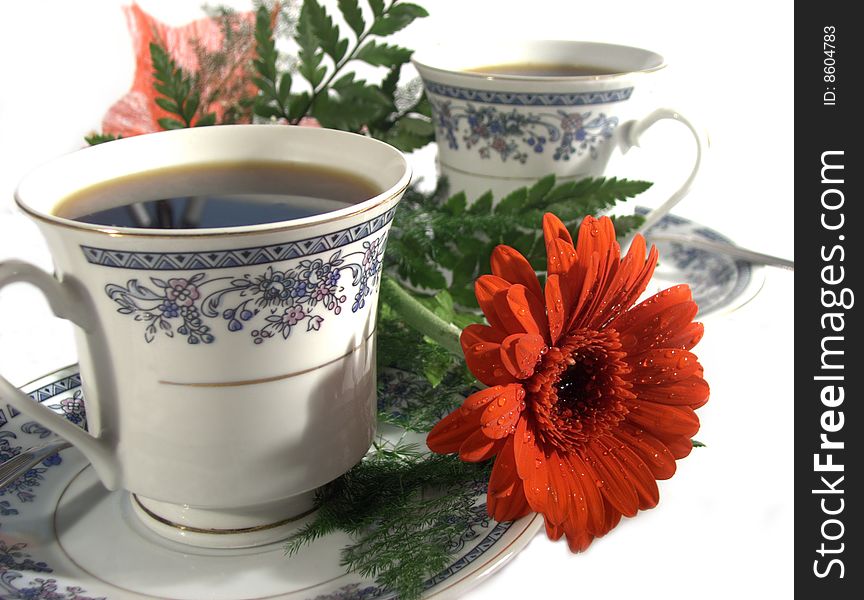 Two coffe cups with one red flower with morning dew or raindrops. Two coffe cups with one red flower with morning dew or raindrops