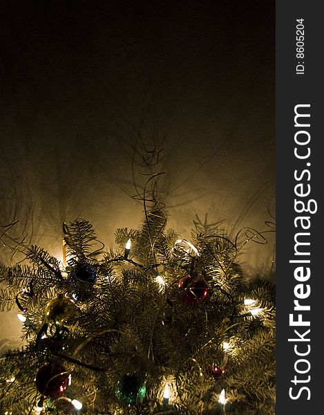 A pine bough decorated with Christmas ornaments and electric lights radiating a warm glow into darkness. A pine bough decorated with Christmas ornaments and electric lights radiating a warm glow into darkness