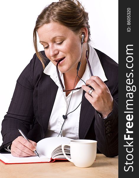 Modern woman writing in notebook with a satisfied expression and handsfree earplug. Modern woman writing in notebook with a satisfied expression and handsfree earplug.