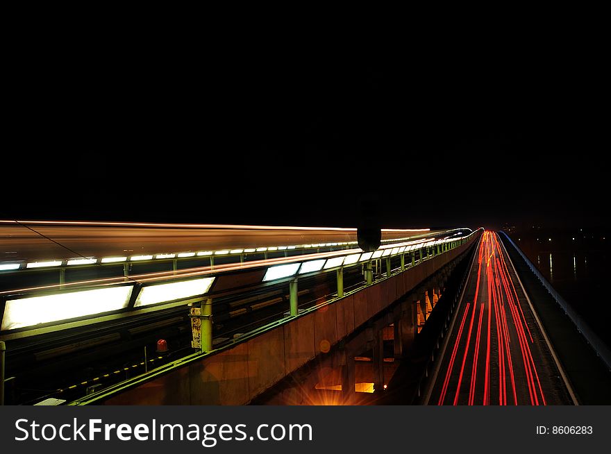 Movement of cars and a train on a city bridge at night. Movement of cars and a train on a city bridge at night