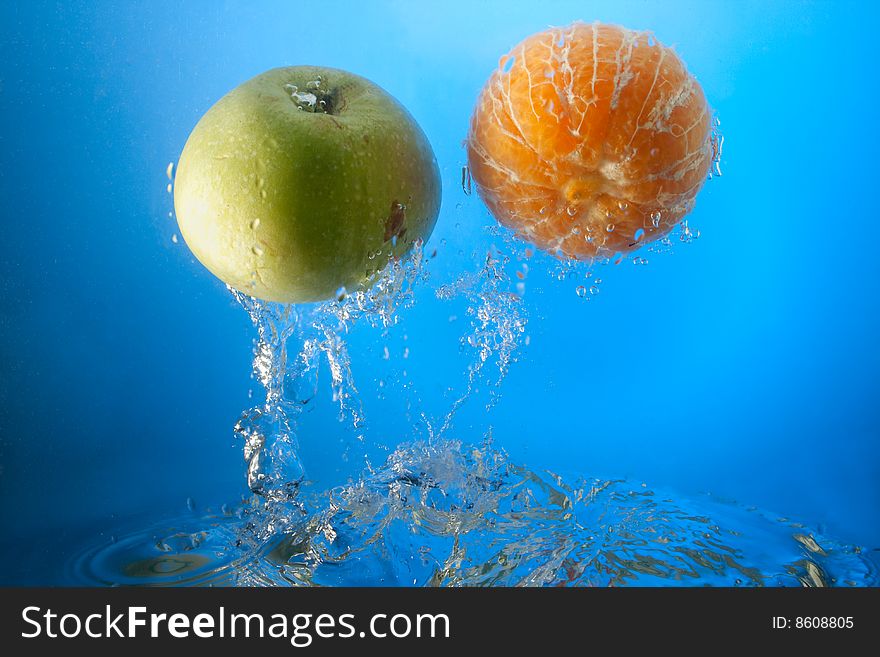 Orange and apple in water, on a blue background