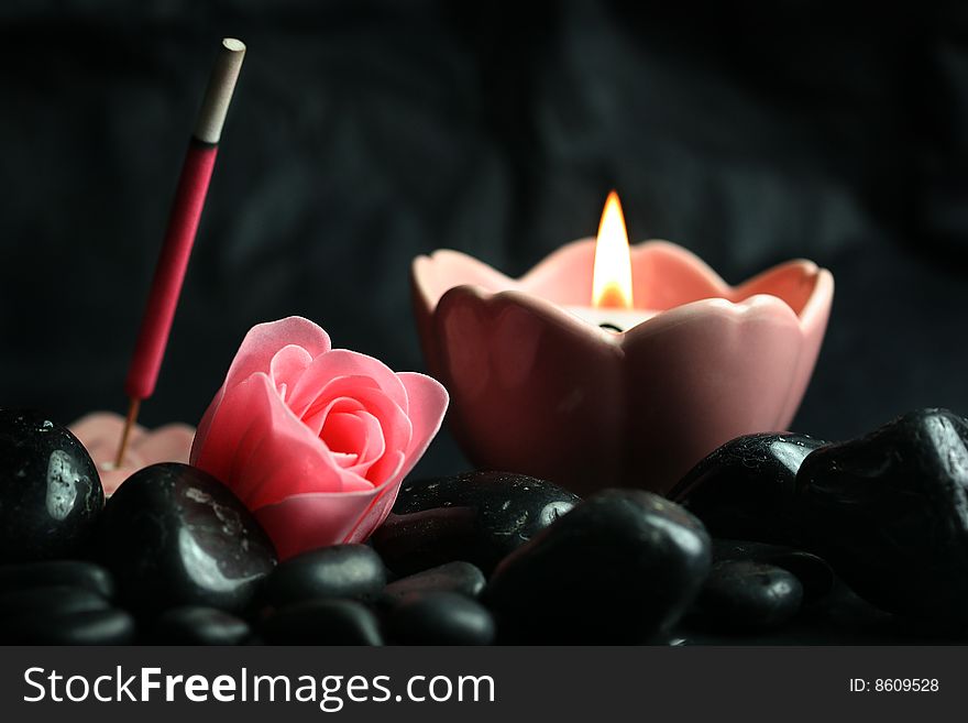 Pink candle and incense burning on black rocks