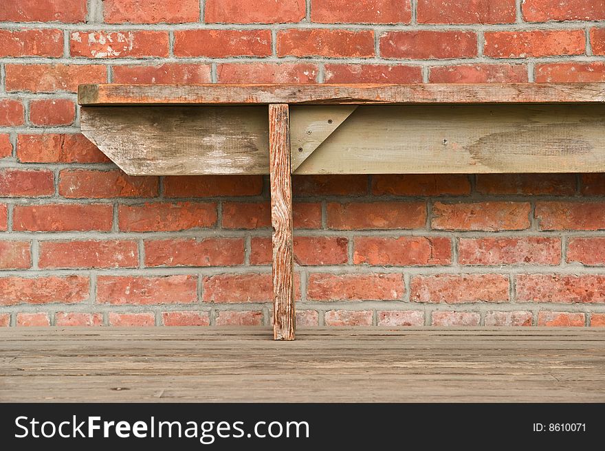 An old wooden bench against a red brick wall. An old wooden bench against a red brick wall