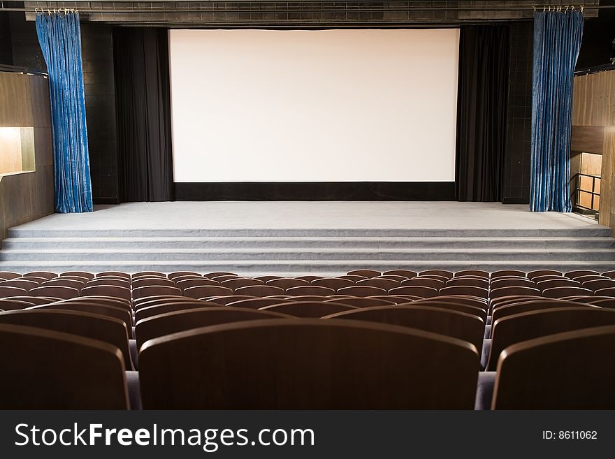 Empty cinema auditorium with line of chairs and stage with silver screen. Ready for adding your own picture. Empty cinema auditorium with line of chairs and stage with silver screen. Ready for adding your own picture.