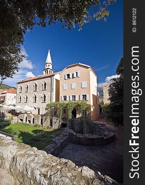 Bell Tower in the Old Town of Budva, Montenegro. Green grass, leaves and blue sky above.