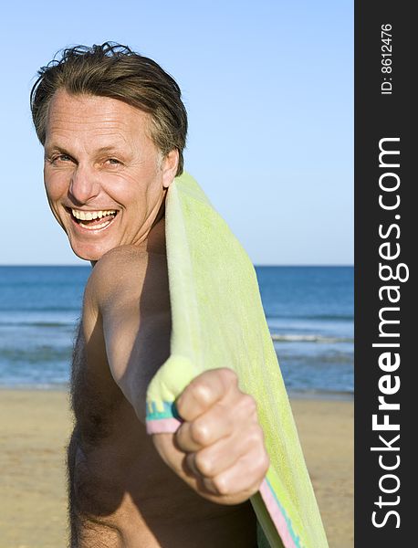 A happy laughing forties man is fooling around with his beach towel on the beach. A happy laughing forties man is fooling around with his beach towel on the beach.