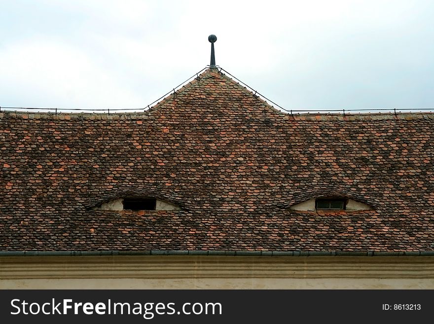 An old roof of tiles from a historic fortress watching sleepy through its windows, in Fagaras, Romania. An old roof of tiles from a historic fortress watching sleepy through its windows, in Fagaras, Romania.