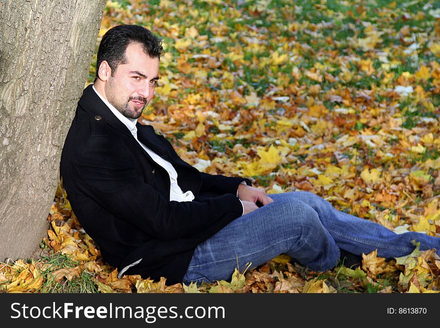 A man sits on the ground leaning the tree. A man sits on the ground leaning the tree