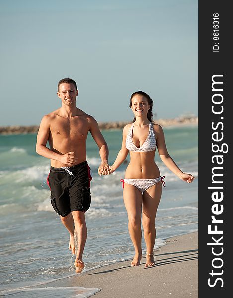 Couple in love holding hands and running on the beach near the water