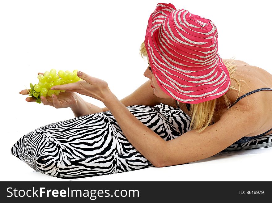 Blond lady in bikini with a summer pink hat and fresh grape, lying on a zebra cushion. White background. Blond lady in bikini with a summer pink hat and fresh grape, lying on a zebra cushion. White background