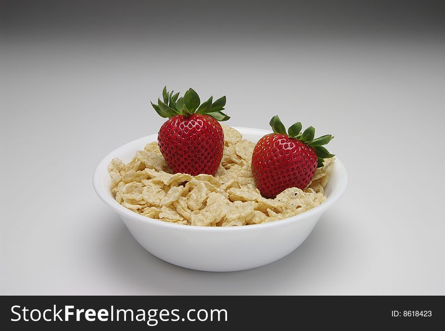 Red and green strawberries with cereal in a white bowl on a white background