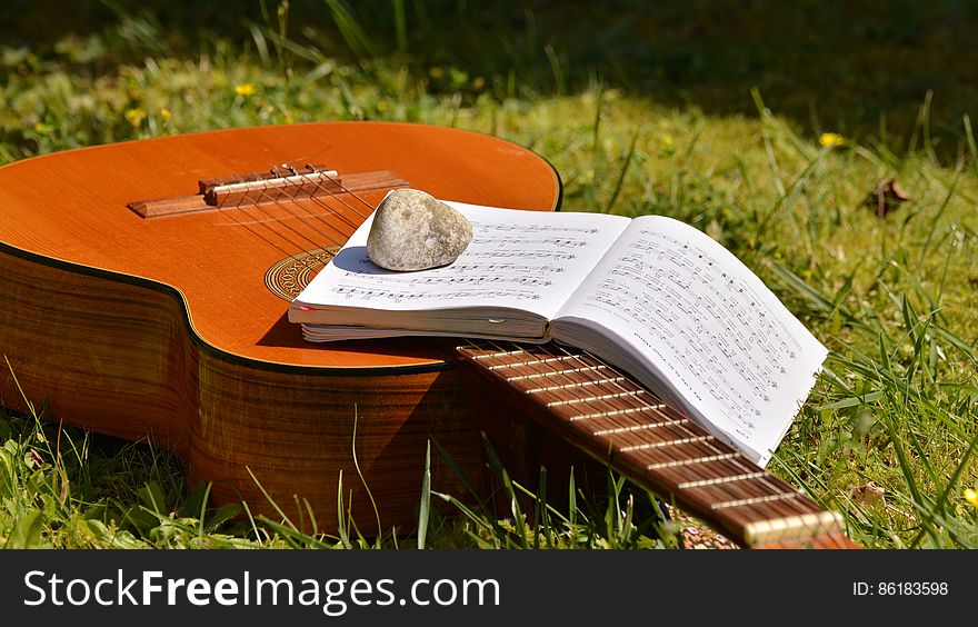 Song Book on Brown Classical Guitar on Green Grass during Daytime