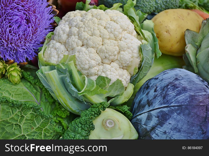 Close up of colorful produce including purple cabbage, cauliflower, potato, broccoli and leafy greens.