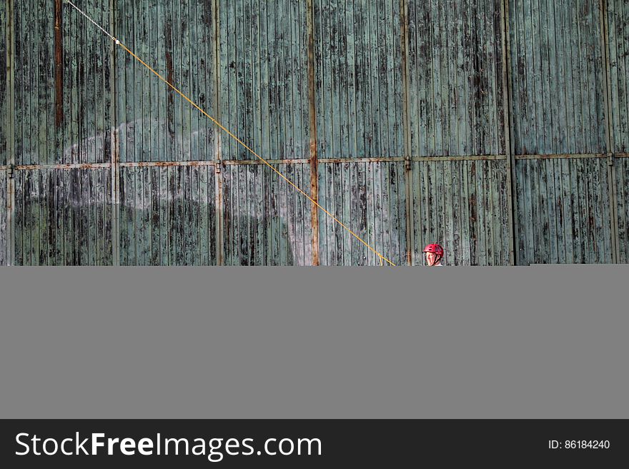 Man on wake board against exterior corrugated metal wall.