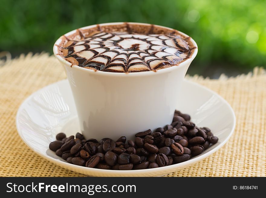 Decorative pattern on cup of coffee outdoors with beans, hessian sack background. Decorative pattern on cup of coffee outdoors with beans, hessian sack background.