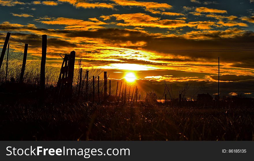 Sunset over country field with silhouette of wooden fence.