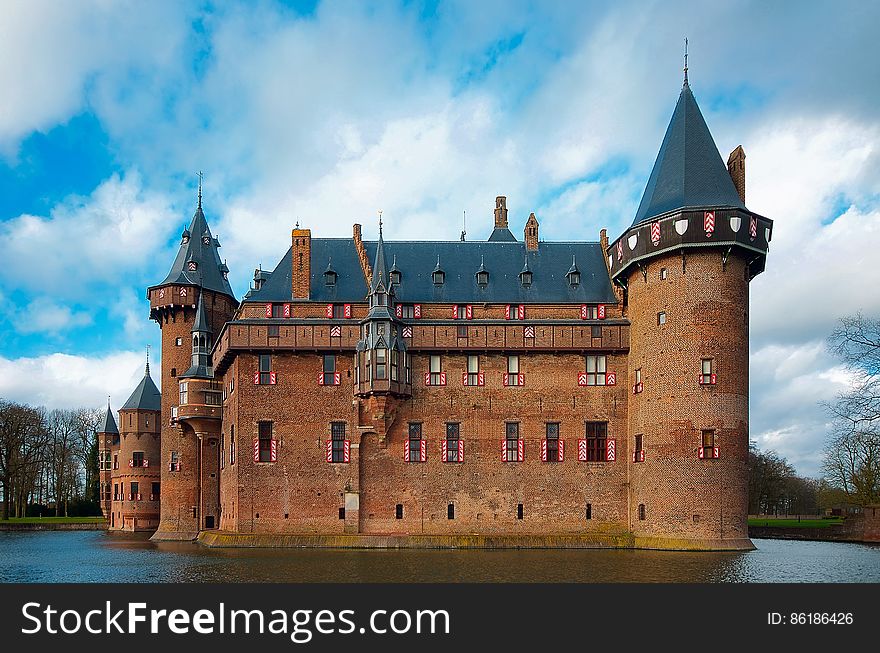 Facade of brick medieval castle surrounded by moat against blue skies with clouds. Facade of brick medieval castle surrounded by moat against blue skies with clouds.