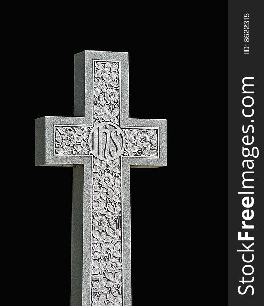 A granite cross (tombstone) with IHS inscription and floral carving on black background. A granite cross (tombstone) with IHS inscription and floral carving on black background.