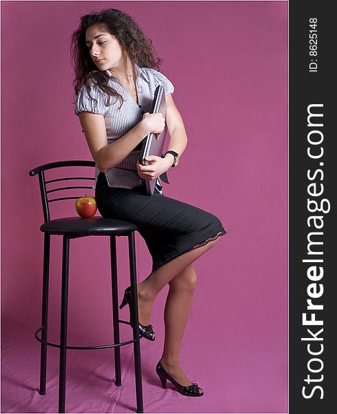 Portrait of young attractive woman sitting full-length on high chair holding a folder with documents, looking aside and down. Portrait of young attractive woman sitting full-length on high chair holding a folder with documents, looking aside and down.