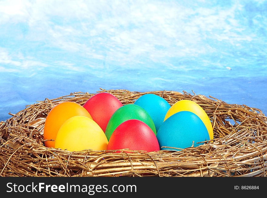 Color eggs in a golden nest on blue sky background