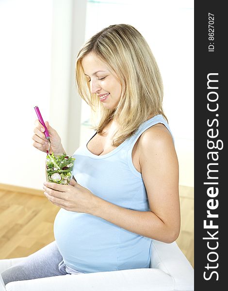 Young pregnant woman is eating salad