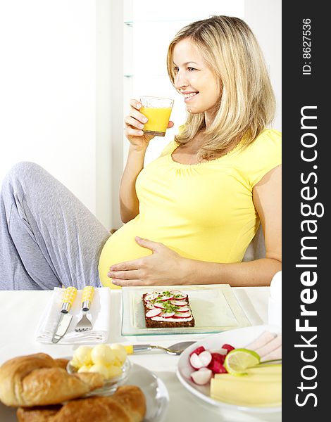 Beautiful young pregnant woman is drinking orange juice