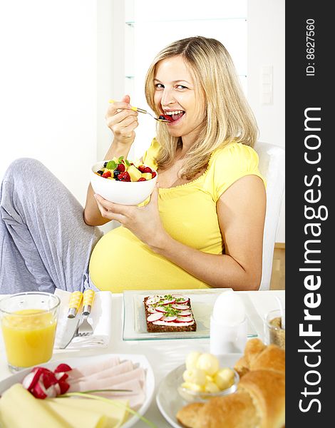 Beautiful young pregnant woman eats fruit salad