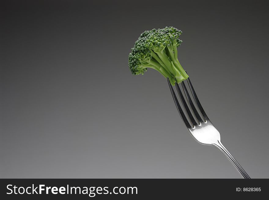 Broccoli stalk on a silver fork, on dark background, horizontal. Broccoli stalk on a silver fork, on dark background, horizontal.