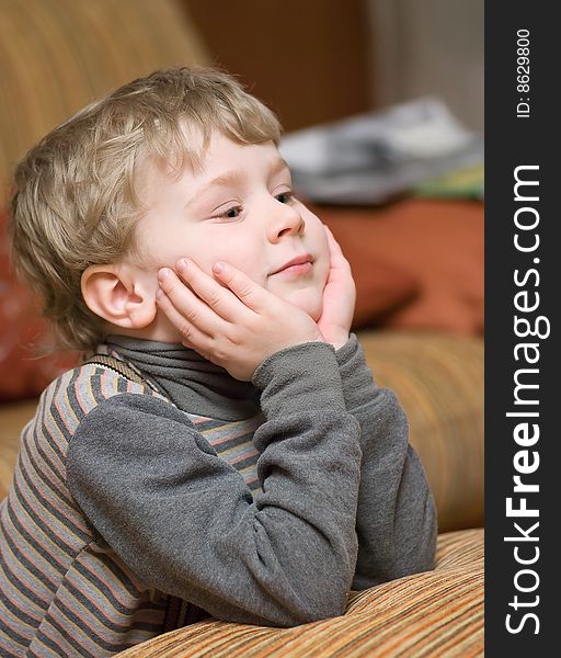 Cute little boy supporting his head with hands and looking at something