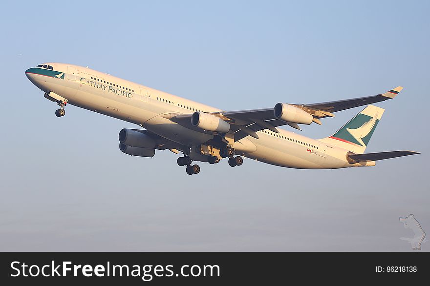 Cathay Pacific plane with cream and blue colors and four jet engines coming in to land, wheels down after a long haul flight, pale blue sky. Cathay Pacific plane with cream and blue colors and four jet engines coming in to land, wheels down after a long haul flight, pale blue sky.