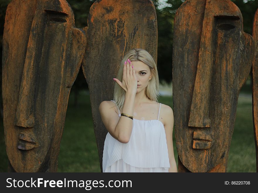 Woman Covering Face With Right Hand in Front of Large Tribal Head Statue