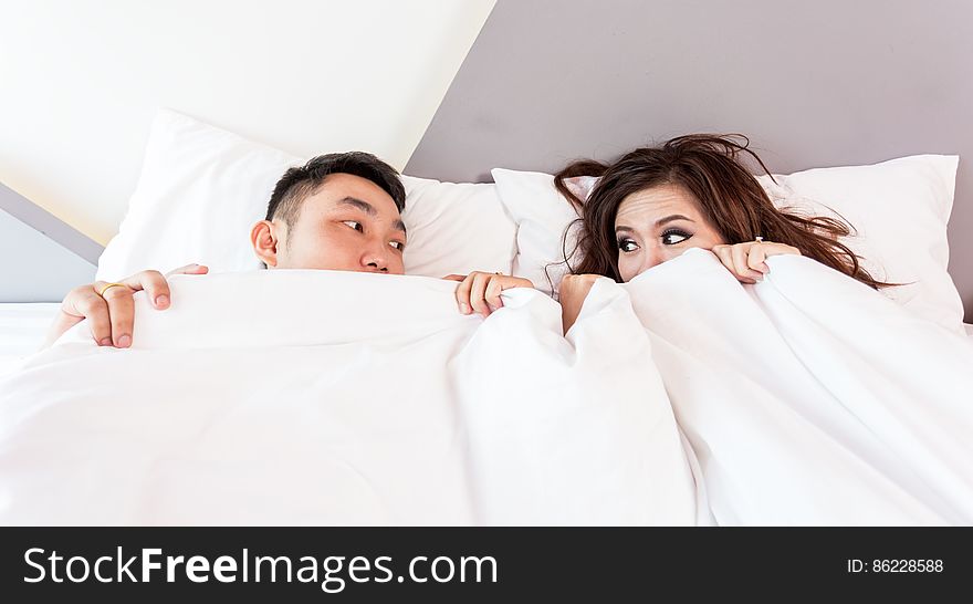 Young Asian couple hiding under white sheets and bedspread in home bedroom. Young Asian couple hiding under white sheets and bedspread in home bedroom.