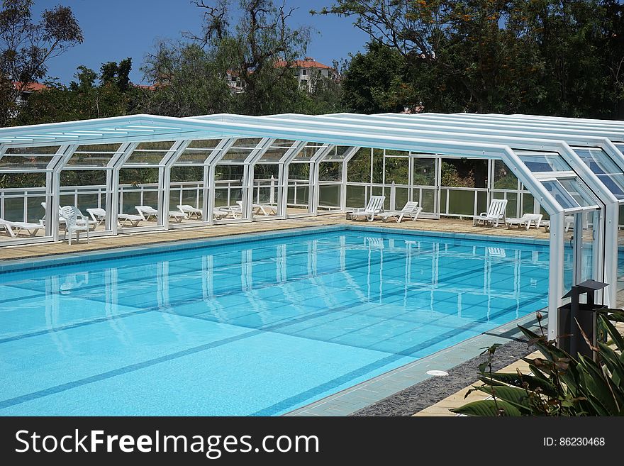 An empty partly covered outdoor swimming pool and sunbeds around. An empty partly covered outdoor swimming pool and sunbeds around.