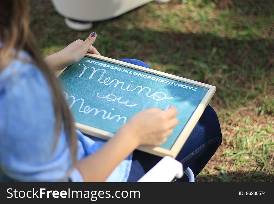 Girl sat outdoors practicing alphabet on chalkboard. Girl sat outdoors practicing alphabet on chalkboard.