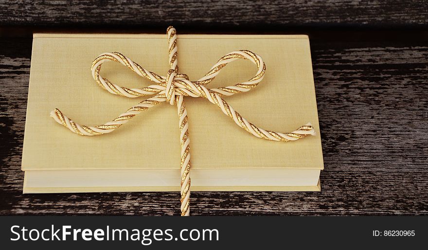 Blank hard cover book tied in gold ribbon on rustic wooden table. Blank hard cover book tied in gold ribbon on rustic wooden table.