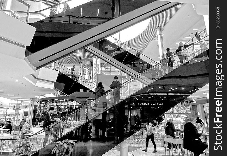 People riding escalator inside modern shopping center in black and white. People riding escalator inside modern shopping center in black and white.