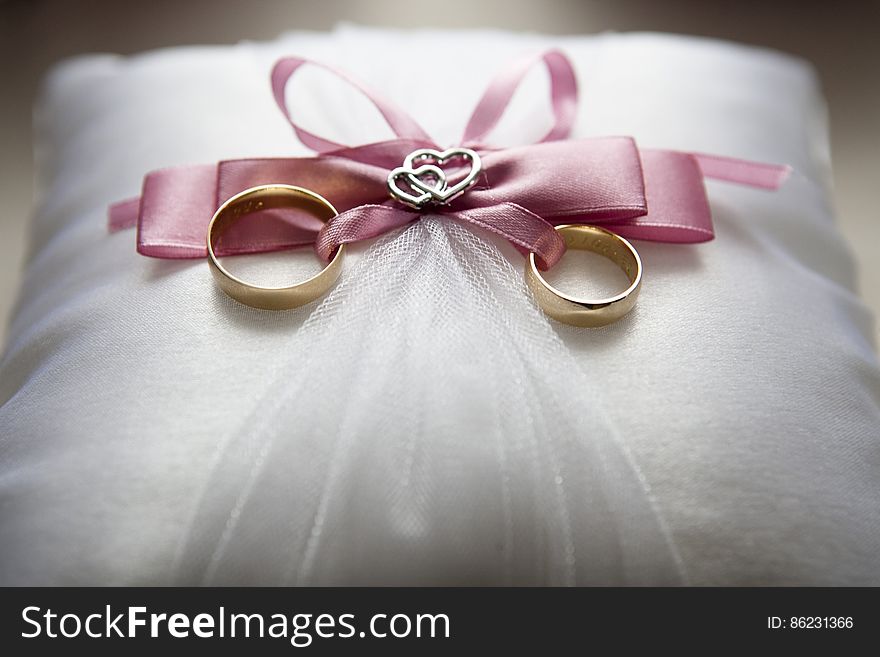 Close up of gold wedding rings on satin pillow with pink bows. Close up of gold wedding rings on satin pillow with pink bows.
