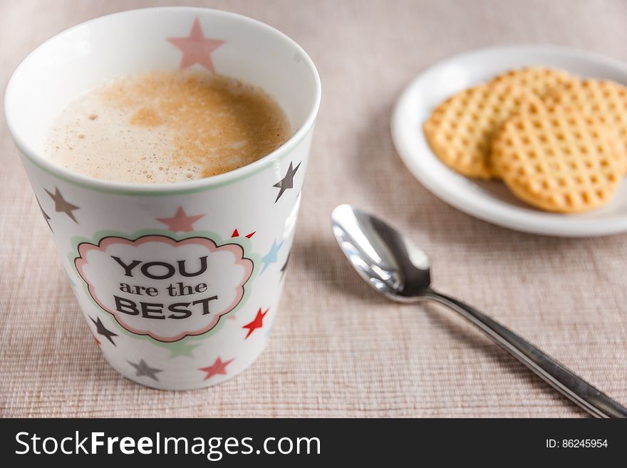 Cup of coffee on table with biscuits and spoon, message reads you are the best.