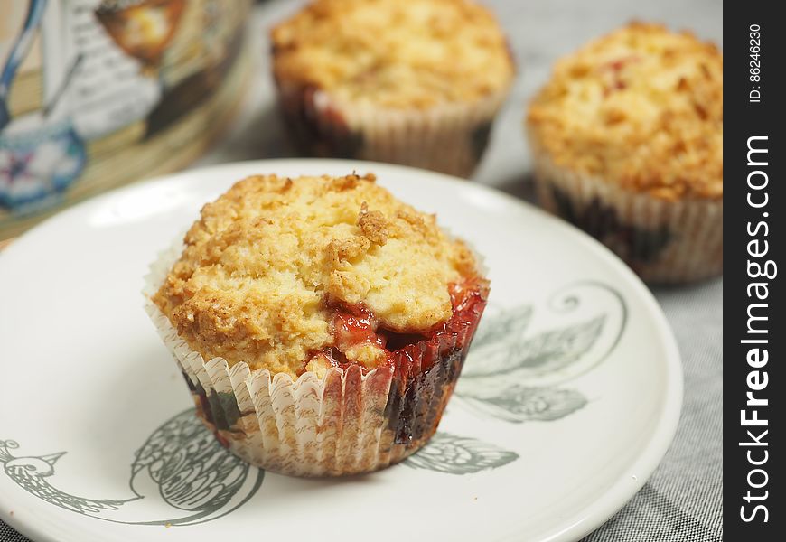 Closeup of freshly baked cherry muffins with one on plate in case.