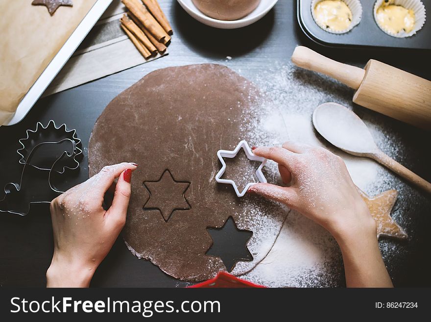 A person cutting ginger bread from piece of dough with a cookie cutter. A person cutting ginger bread from piece of dough with a cookie cutter.