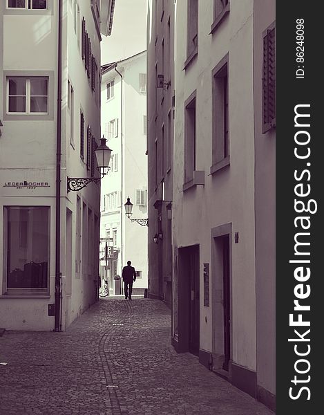A monochrome photo of a man walking along a cobbled alley in an old town. A monochrome photo of a man walking along a cobbled alley in an old town.
