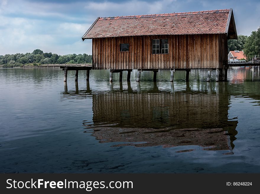 Wooden boathouse on stilts reflecting in waters on sunny day. Wooden boathouse on stilts reflecting in waters on sunny day.