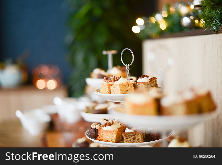 Pieces of iced cakes laid out on plates with selective focus two particular slices and a Christmas tree in the blurred background. Pieces of iced cakes laid out on plates with selective focus two particular slices and a Christmas tree in the blurred background.