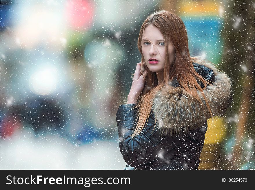 Attractive young woman in a Winter coat with large fur collar posing while snow is falling. Attractive young woman in a Winter coat with large fur collar posing while snow is falling.
