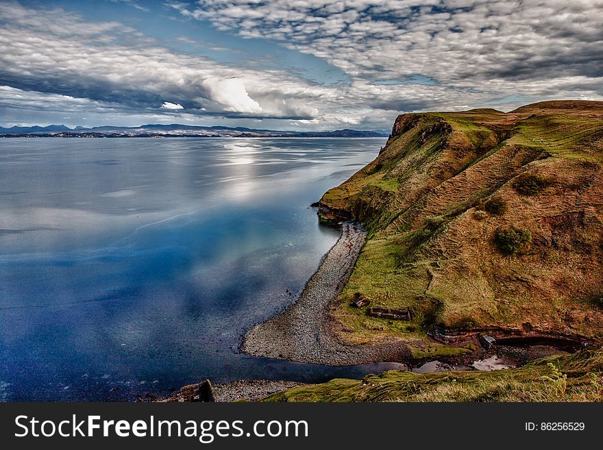 Cliff over waterfront against blue skies with clouds on sunny day.