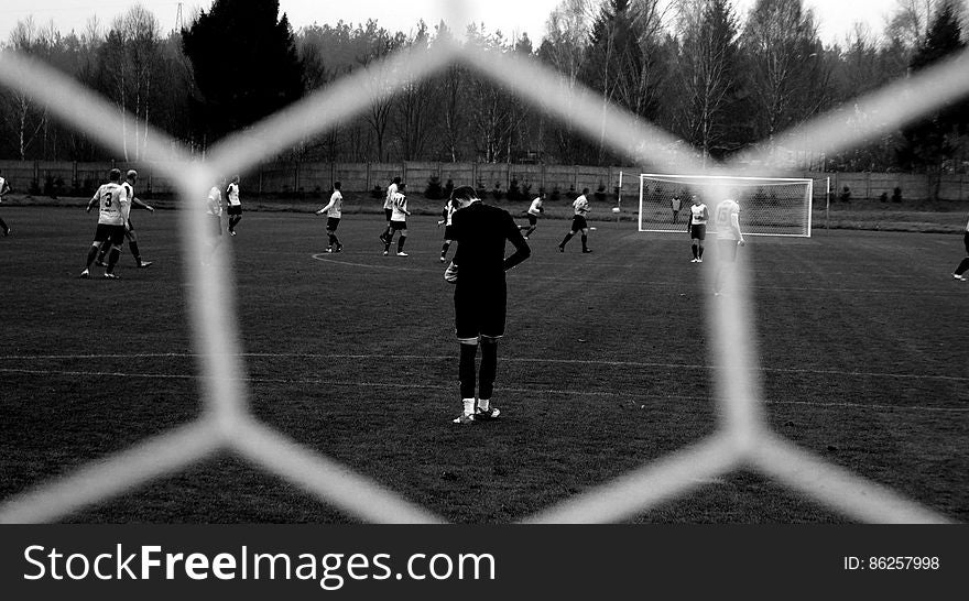 Players on soccer field through mesh net in black and white. Players on soccer field through mesh net in black and white.