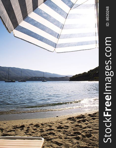 View of an umbrella on a greek beach and yachts at the background, under the summer sun.